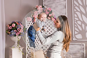 Young mother holding her newborn child. Woman and baby boy relax in a white bedroom. Nursery interior. Family at home