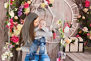 Young mother holding her newborn child. Woman and baby boy relax in a white bedroom. Nursery interior. Family at home