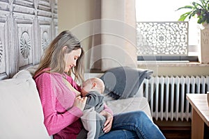 Young mother, holding her toddler boy, breastfeeding him at home