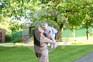 Young mother holding little female baby in garden.