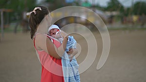 Young mother holding and playing with her baby boy child in city park standing wearing bright red dress - Son wears