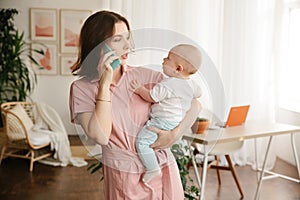 A young mother holds a baby in her arms and talks on the phone