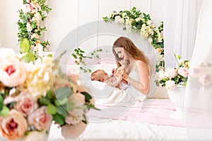 A young mother holds a child in her arms and kisses its legs in a beautiful interior, the concept of love and care of the mother