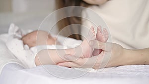 Young mother holds in her arms the little feet of a newborn. Baby sleeps in a cradle next to mom