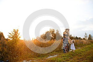 A young mother holds her daughter`s hands and looks at her, standing on a country road at sunset