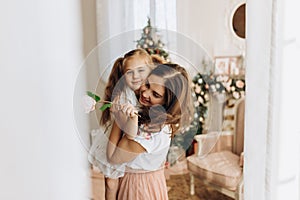 Young mother holds on her hands her little daughter in the cozy room with the New Year`s tree