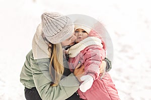 Young mother holds her little daughter in her arms and kisses her. Family portrait. Motherhood and childhood