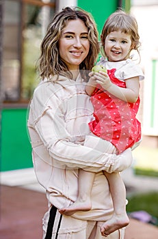 Young mother holds her little daughter on her hands in the garden on a warm summer day