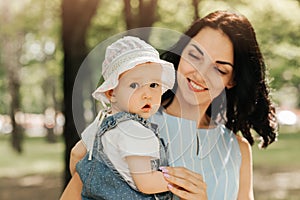 A young mother holds the little daughter infant in the park in the summer