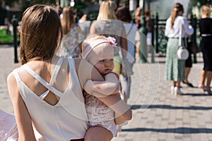 Young mother holds little doughter walking down the street. Back view photo