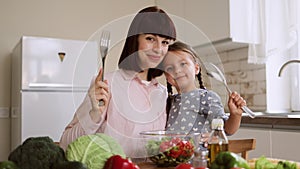Young mother hugging her child daughter and looking at each other holding a spoon and fork