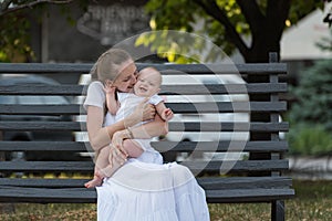 Young mother hugging and kissing baby sitting on Park bench. long-awaited first child