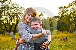 Young mother hugging and kissing her son in summer or autumn park. Family love first. Happy family of mother and child on field at