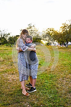 Young mother hugging and kissing her son in summer or autumn park. Family love first. Happy family of mother and child on field at