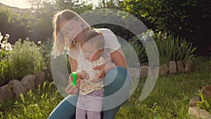 A young mother hugs her little girl, who is learning to blow soap bubbles. Slow motion. Summertime. The concept of child