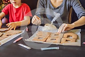 Young mother and kid making gingerbread house on Christmas eve