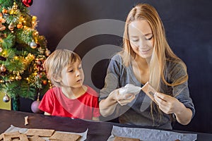 Young mother and kid making gingerbread house on Christmas eve