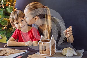 Young mother and kid making gingerbread house on Christmas eve