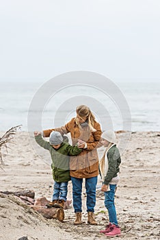 young mother and kids spending time together on seashore on cold