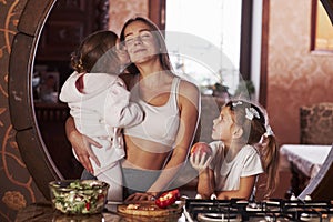 Young mother with kids standing in the kitchen and have some fun