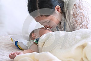 Young mother kiss her cute little baby face with love while her son sleeping on the bed. Motherâ€™s day concept