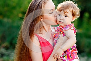 Young mother kissing baby daughter in park