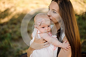 Young mother kissing cute baby girl walking in park