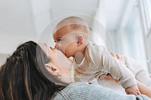 Young mother kissing her cute baby boy on hands in bright room love emotion