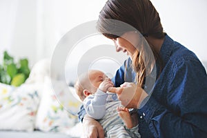 Young mother, kissing her newborn baby boy at home