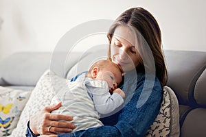 Young mother, kissing her newborn baby boy at home