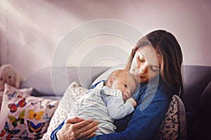 Young mother, kissing her newborn baby boy at home