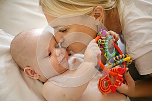 Young mother kissing and playing with her baby boy at home.