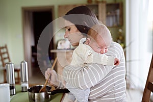 Young mother in kitchen holding baby son, cooking