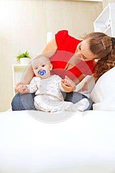Young mother laying on couch and playing with baby