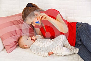 Young mother laying on sofa and playing with baby