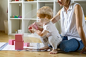 Young mother and little baby assembling pink cube Maria Montessori ecological materials