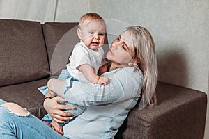 Young mother with little baby daughter  on sofa at home the baby crying mom soothes