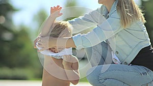 A young mother with a little blond son playing on the lawn and reading a book near the pool.