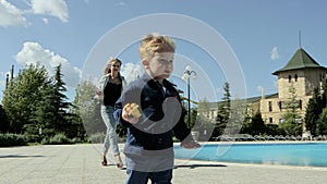 A young mother with a little blond son playing on the lawn and reading a book near the pool.