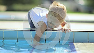 A young mother with a little blond son playing on the lawn and reading a book near the pool.