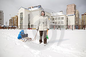 Young mother and little boy enjoying sleigh ride. Child sledding. Toddler kid riding sledge. Children play outdoors in snow. Kids