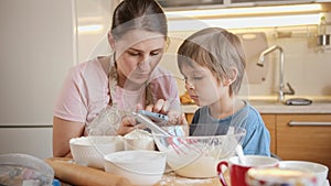 Young mother with little boy looking in recipe on smartphone for making biscuit at home. Children cooking with parents