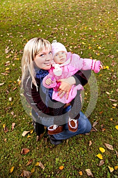 Young mother and little child sitiing on grass in autumn park.