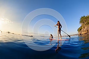 Young mother with little clild paddling on stand up paddleboard