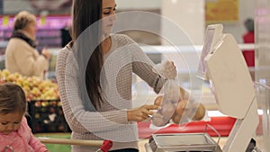 Young mother with little daugher weighting vegetables and fruits in supermarket