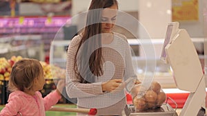 Young mother with little daugher weighting vegetables and fruits in supermarket