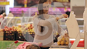 Young mother with little daugher weighting vegetables and fruits in supermarket