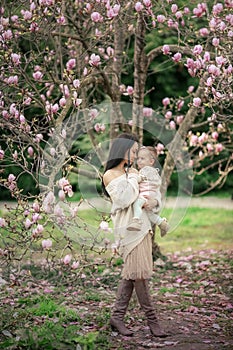 Young mother and little daughter in autumn park play with magnolia leaves. Happy weekend with family in autumnal forest