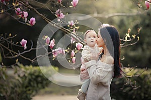 Young mother and little daughter in autumn park play with magnolia leaves. Happy weekend with family in autumnal forest