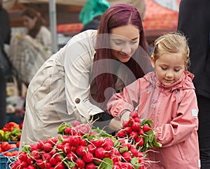 Young mother with little daughter buying fresh radishes